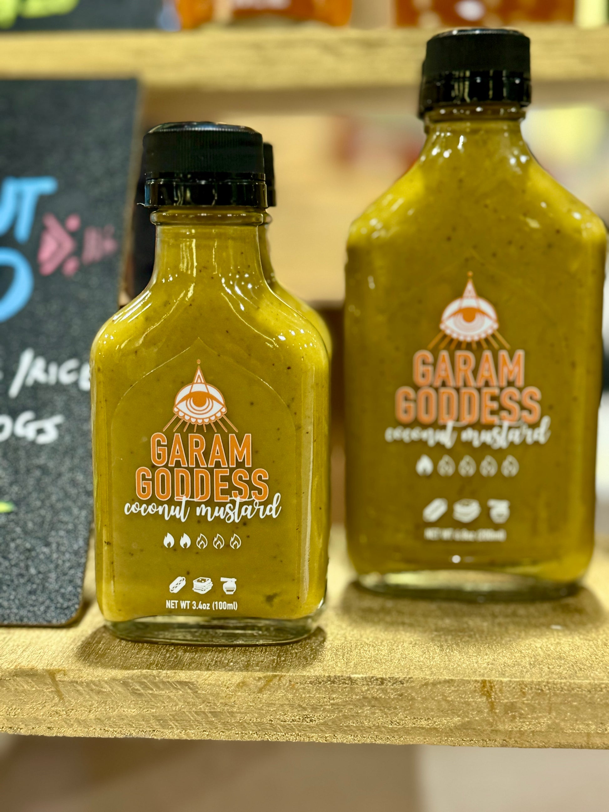 Garam Goddess Coconut Mustard hot sauce bottle with creamy white label, showcasing its unique blend of flavors.  The vegan and gluten-free profile includes clean ingredients like scotch bonnet peppers, tender coconut, cilantro, garlic, curry leaves and mustard seeds.