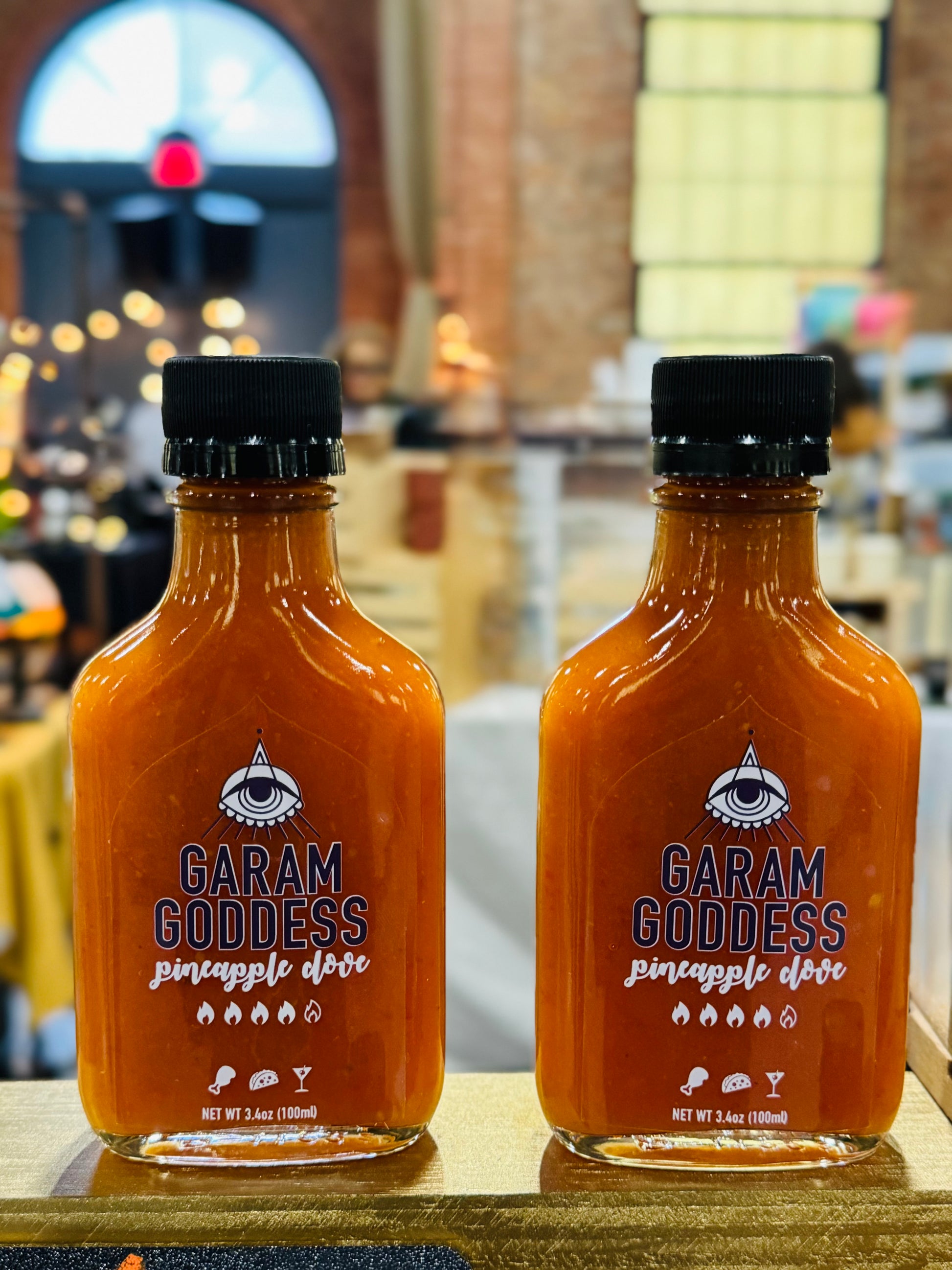 Two Garam Goddess Pineapple Clove hot sauce bottles with bright yellow label, indicating its briny and spicy, vegan, and gluten-free composition. Highlighting ingredients like habanero peppers, garlic, cloves lacto-fermented.